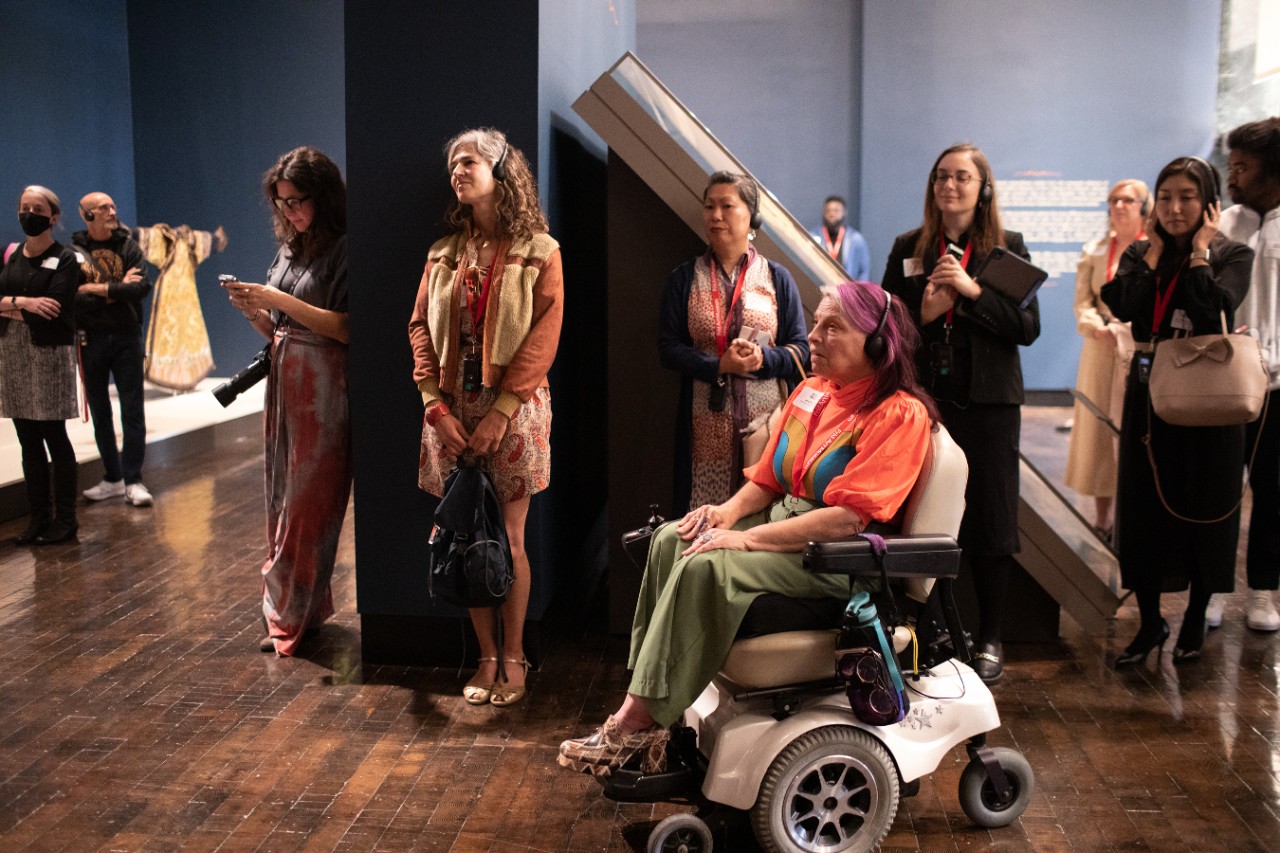Splendor preview-16 several patrons, including a woman in a power wheelchair (Alicia Searcy), gather in the museum with headphones on to listen to the audio tour of the artwork