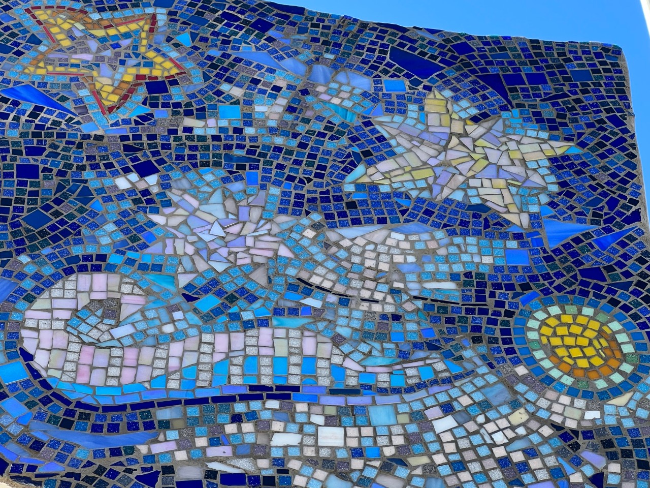 Closer look at "Positive Space" a detailed image of the blue mosaic sculpture depicting a sun, stars of differing sizes, waves and curls, etc.