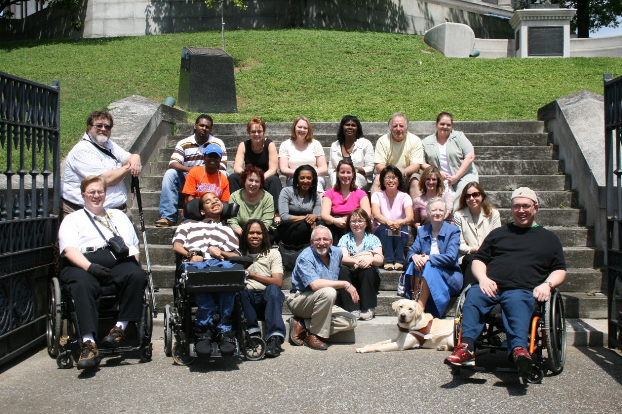 Partners Class of 2008 A large banner photo with the article headline shows a diverse group of people, some in wheelchairs, one with a cane, one with a service dog, posing around a set of stone stairs and smiling at the camera.