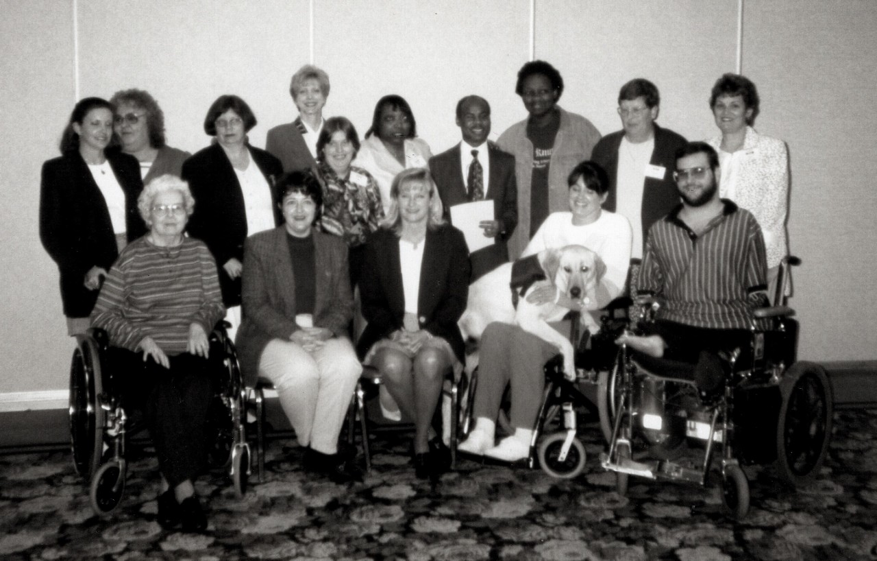 Partners Class of 1998 a black-and-white photo of a posed group of 15 people, some in wheelchairs, one with a service dog