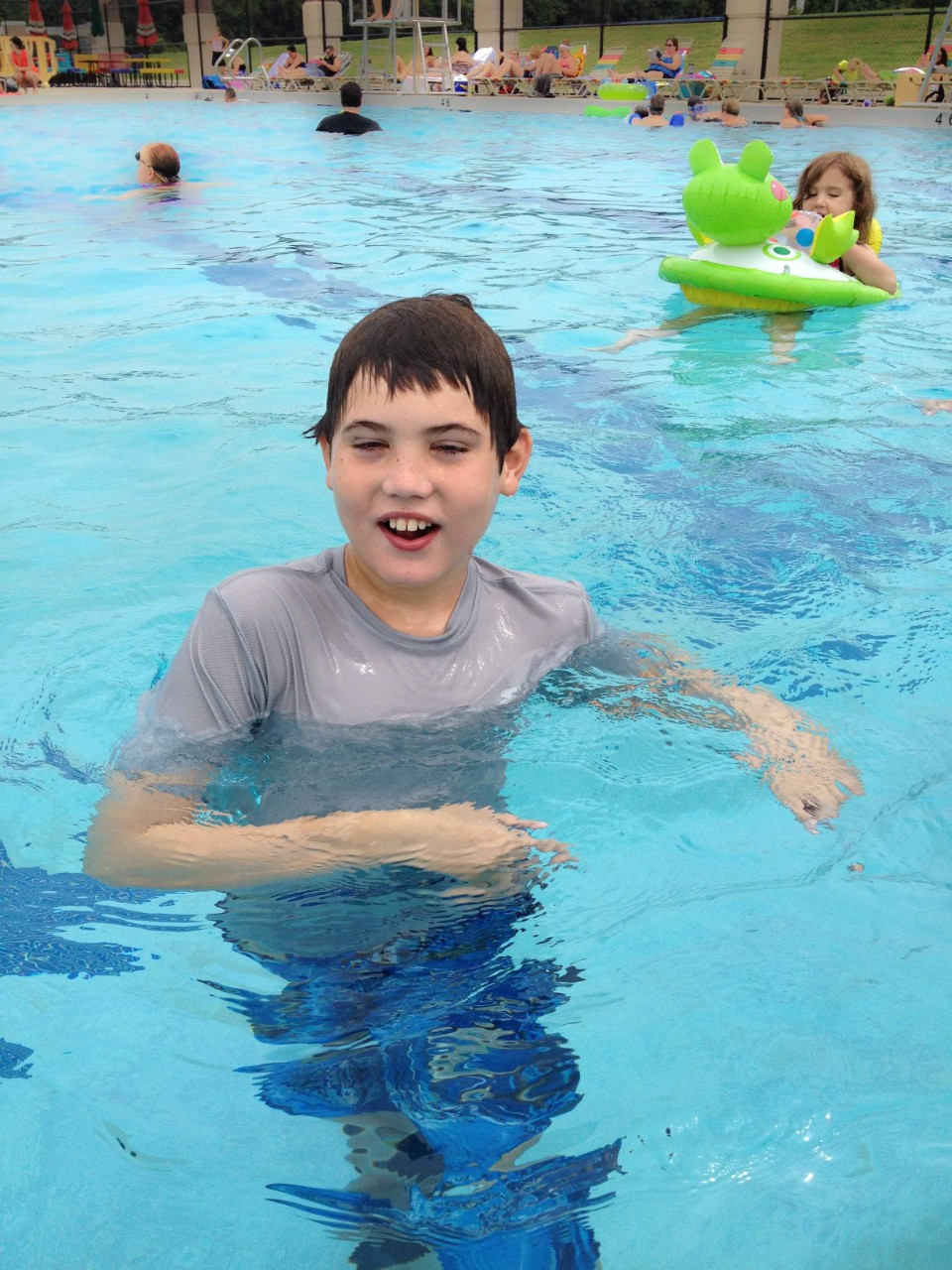 Photo by Jen Vogus a young boy is swimming in a big public pool. He is obviously very happy to be in the water.