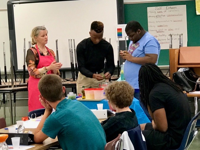 several people in a classroom standing around a table, working on a food preparation activity