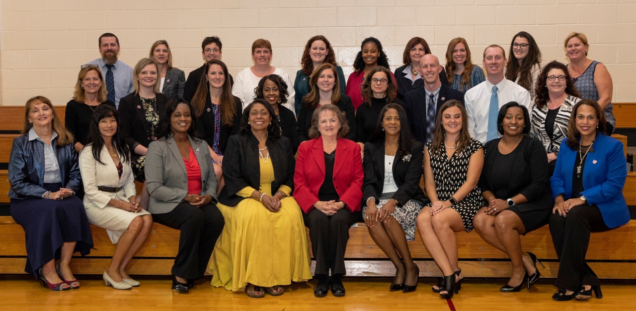 group photo of a diverse group of about 30 adults who are state employees, sitting together on gym bleachers