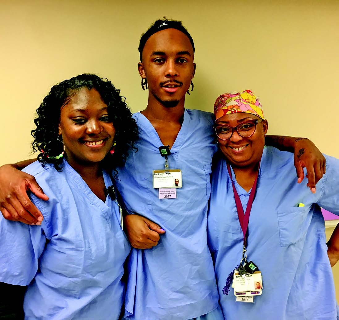 Project SEARCH at Progress: Ron with coworkers Raykeyda and Ms. Z three African American people, co-workers, with arms around each other. They are all wearing blue hospital scrubs. They are, left to right, Raykeyda, Ronand Ms. Z.