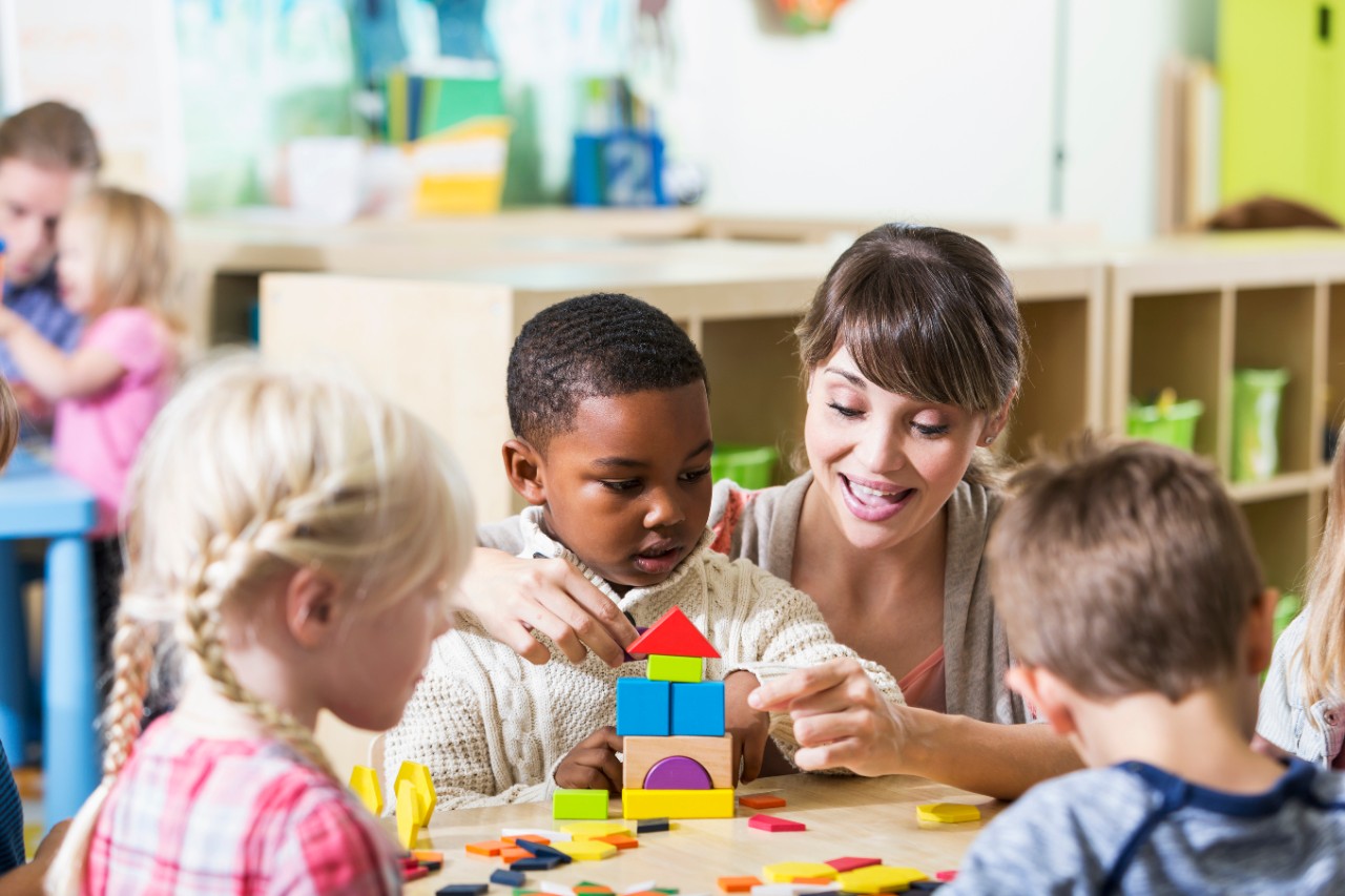 Child Care Teacher helps young children with building blocks at daycare