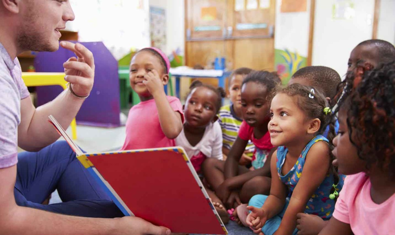 Male teacher reading book to young children
