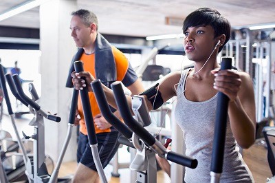 494810207 man and woman next to each other on elliptical machines in gym
